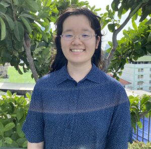 A headshot of Mahiro Noda'26, standing in front of trees in her apartment balcony in Thailand, where she lived before coming to Grinnell.